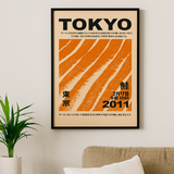 Framed poster with 'TOKYO' text and orange design on a wall above a sofa.