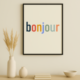 Framed poster with 'bonjour' in multicolor on a wall above a wooden cabinet.