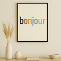 Framed poster with 'bonjour' in multicolor on a wall above a wooden cabinet.