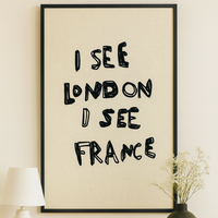 Framed artwork with text 'I SEE LONDON I SEE FRANCE' on a wall above a wooden table.