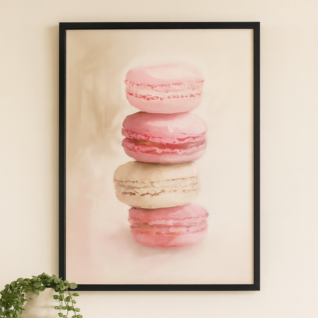 Framed artwork of pink macarons on a wall above a white cabinet.